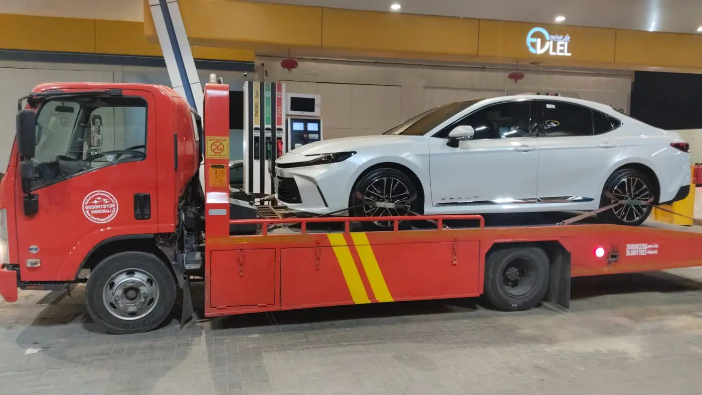 سطحة حمراء تنقل سيارة كامري في محطة وقود في الخرج